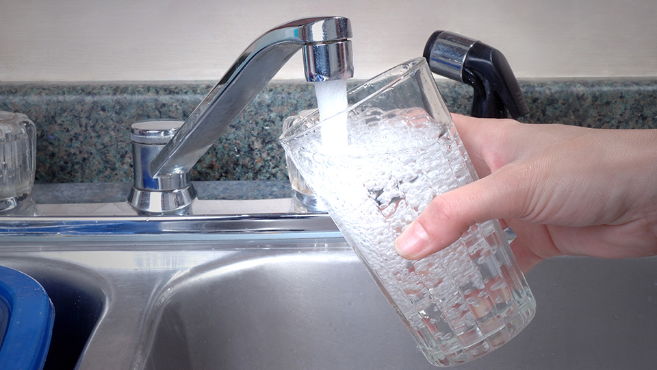 Hand som håller i ett glas och häller upp dricksvatten från vattenkranen.