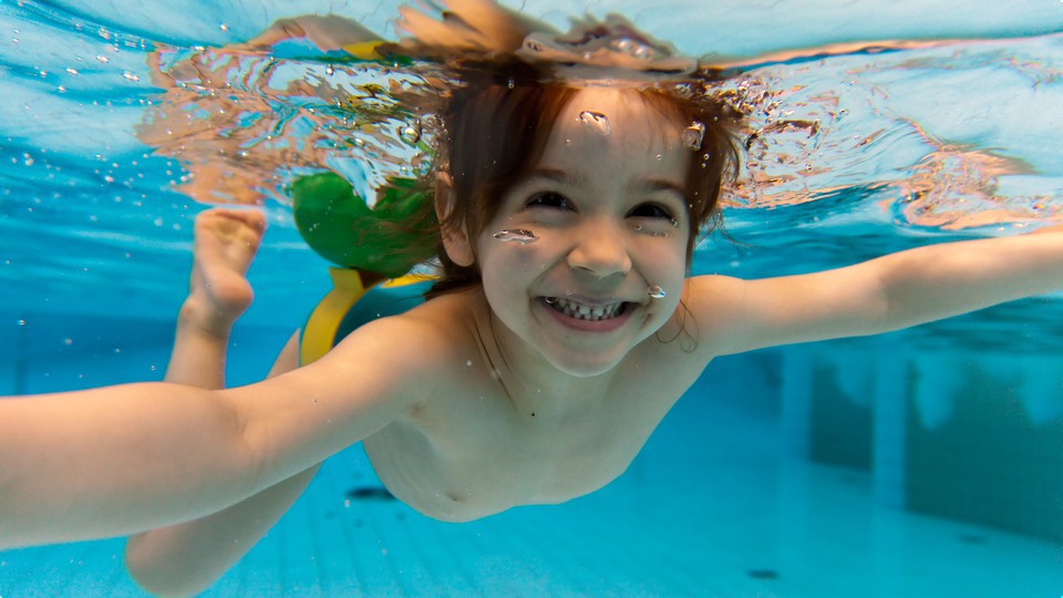 Barn som ler under vattnet i simbassäng.