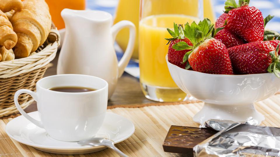 Lyxigt frukostbord med kaffe, juice, bröd, jordgubbar och choklad.
