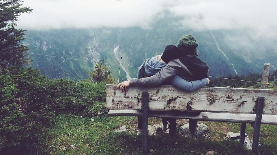 Par som sitter på en bänk och tittar på en utsikt över en dalgång
