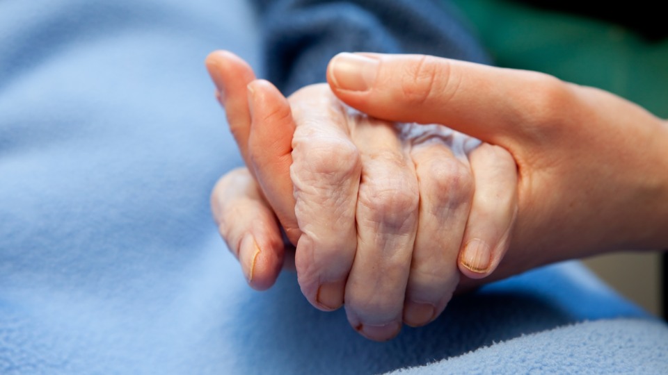 En äldre persons hand håller en yngre persons hand