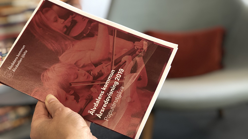 En hand som håller i en broschyr, Årsredovisning 2019 för Älvdalens kommun, en populärutgåva 
