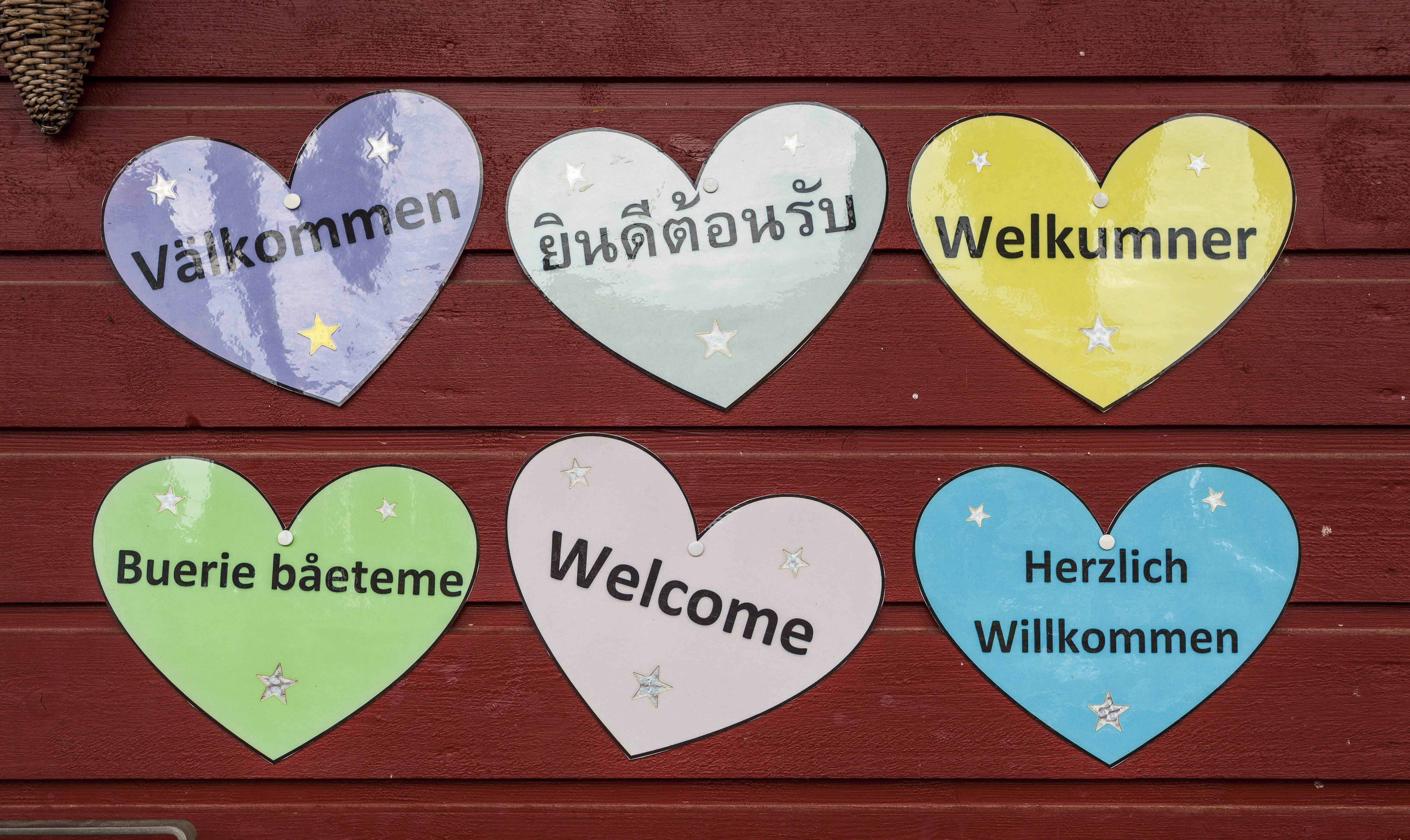 Hjärtan uppsatta på husvägg med texten välkommen på olika språk.