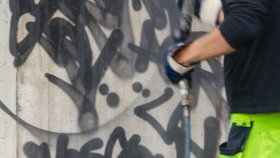 Detaljbild på arm som håller i en högtryckstvätt och tar bort klotter på en vägg