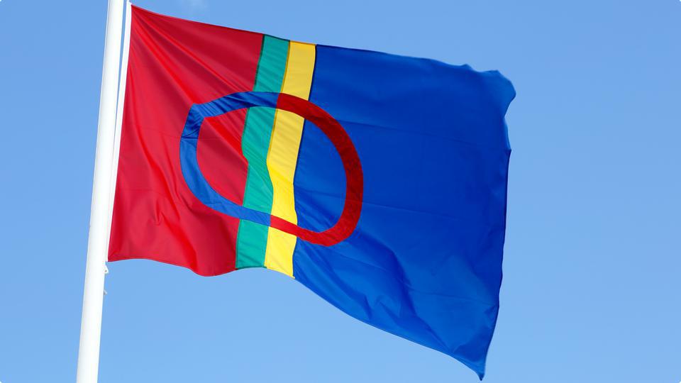 Närbild av samernas flagga mot blå himmel.