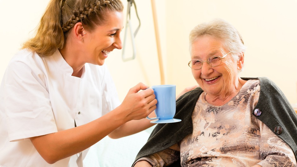 Ung sköterska ger äldre brukare en kopp kaffe.