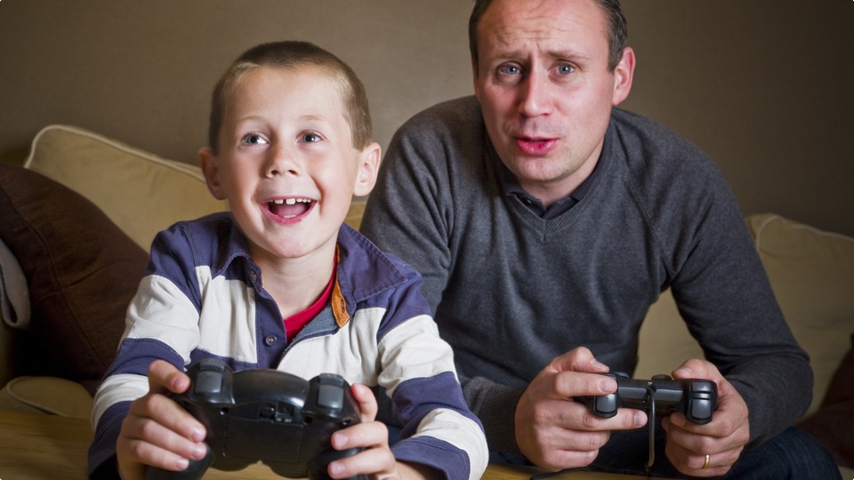 Glad man och pojke sitter i soffa och spelar dataspel.