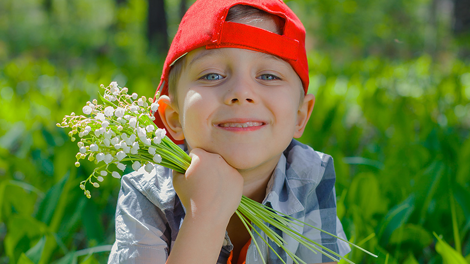 Glad pojke med röd keps som håller i en bukett med liljekonvaljer