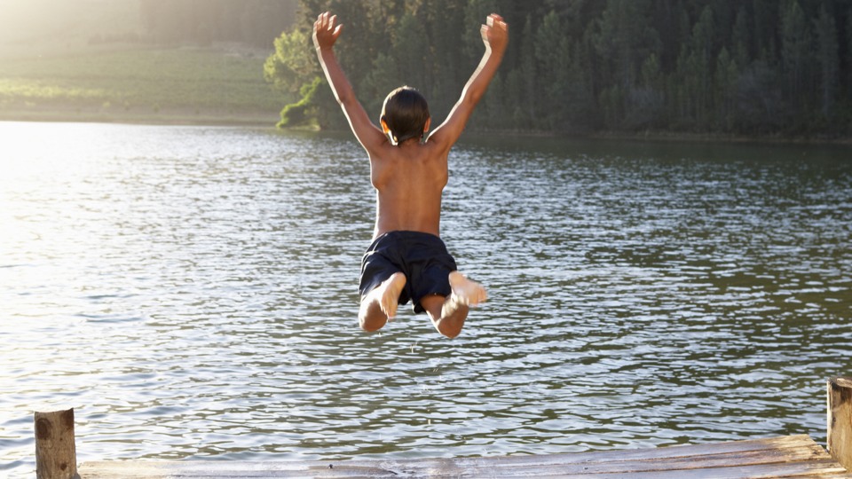 Barn hoppar i sjö från träbrygga