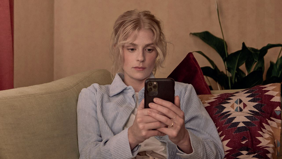 Kvinna som sitter i en soffa och tittar på en mobiltelefon