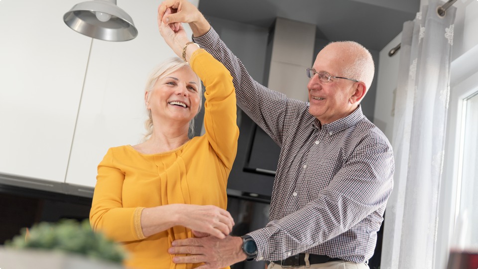 Äldre par dansar och har trevligt tillsammans i köket.