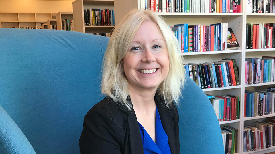 Karin Rytter sitter i en blå fotölj med bokhyllor i bakgrunden
