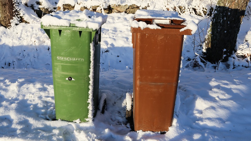 En grön och en brun soptunna vid vägen en snöig vinterdag.