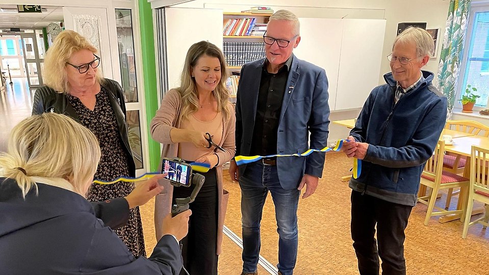 Ett antal personer deltar vid invigning av närsjukvårdsplats på Särna vårdcentral där en person klipper det blågula bandet.