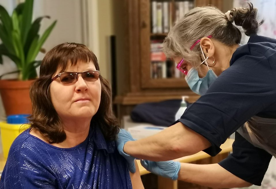 En kvinnlig vårdpersonal får sin första vaccinspruta mot covid-19 av vaccinatör.
